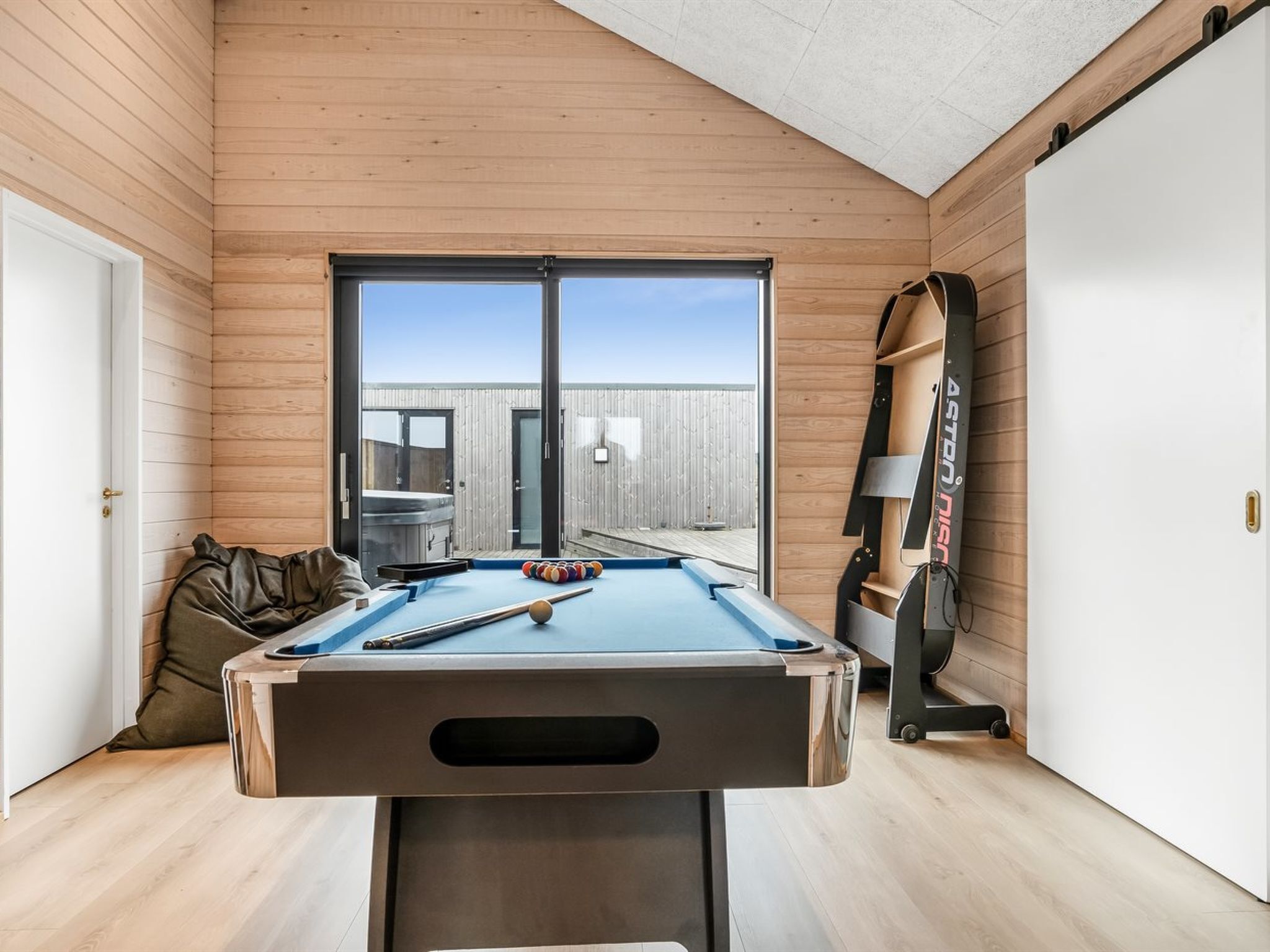 A pool table in a room with wooden walls and a large window.