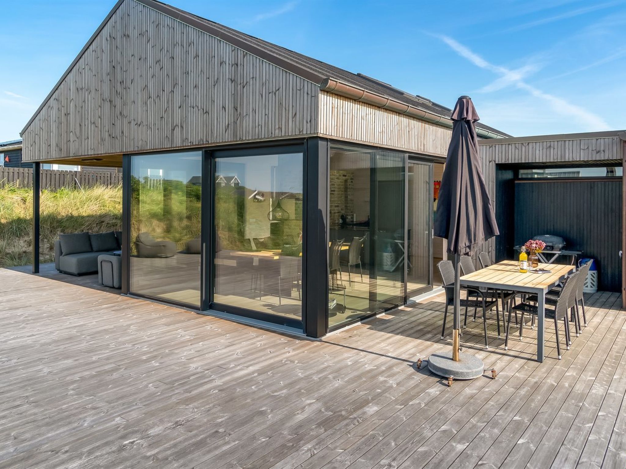 A modern house with a large glass door, a deck with outdoor furniture, and a barbecue area.