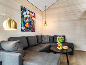 Ein modernes Wohnzimmer mit einem Ecksofa, einem runden Couchtisch mit Obstschalen, einem farbenfrohen abstrakten Gemälde und einer Pendelleuchte.