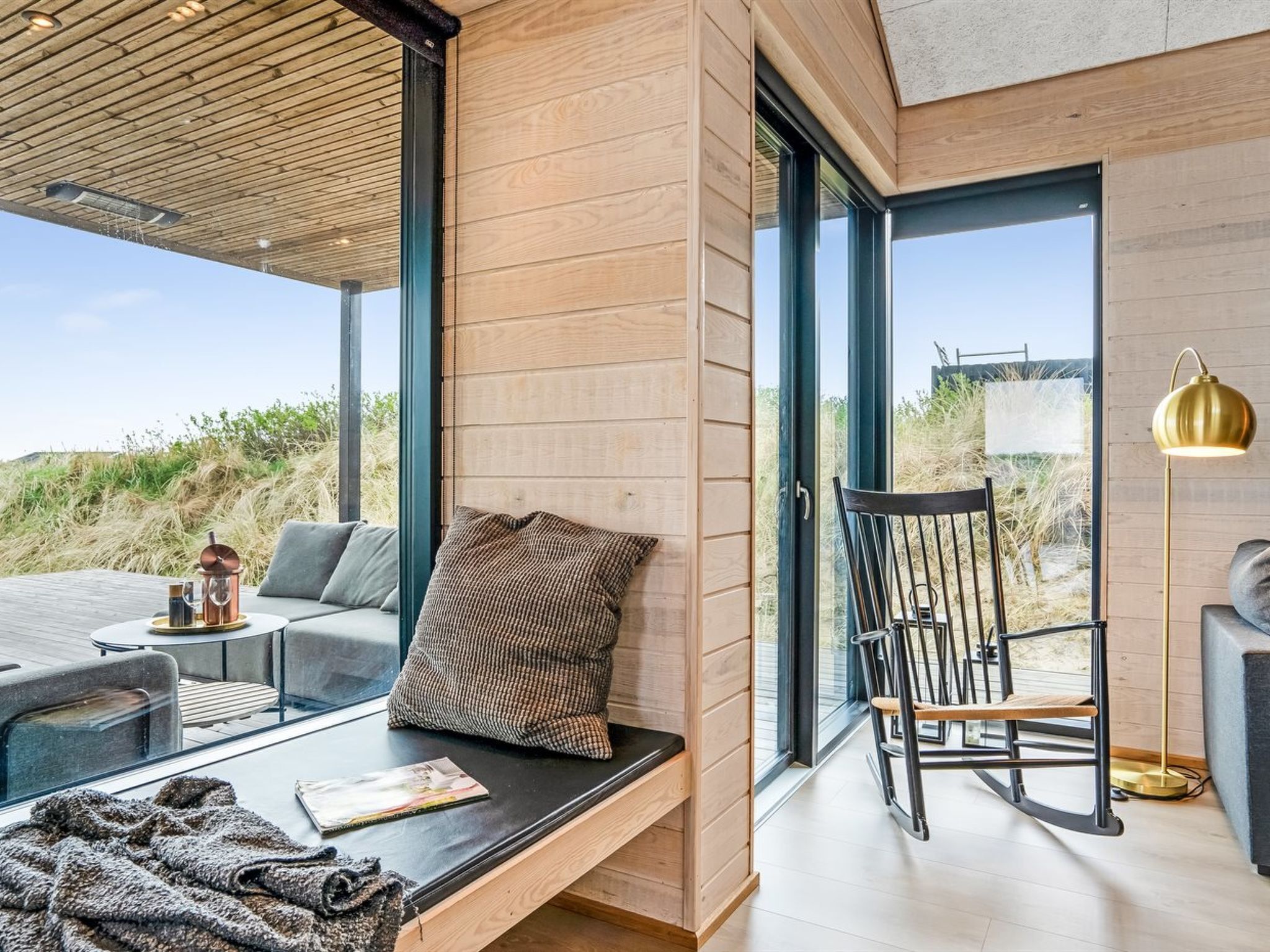 Un intérieur moderne avec un banc en bois, un fauteuil à bascule et une table en verre.