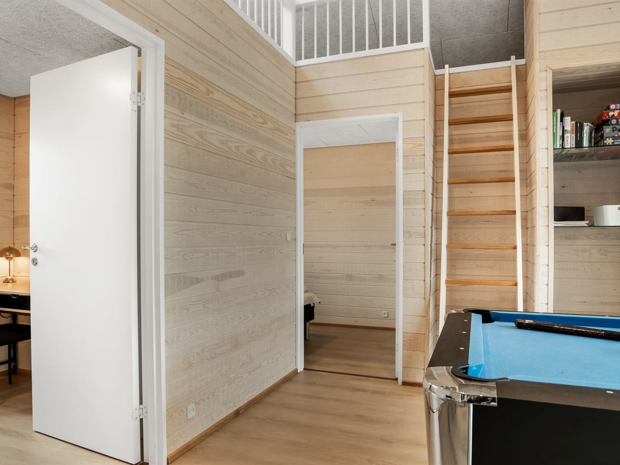 Een kamer met een pooltafel, houten wanden, een witte deur en een boekenplank.