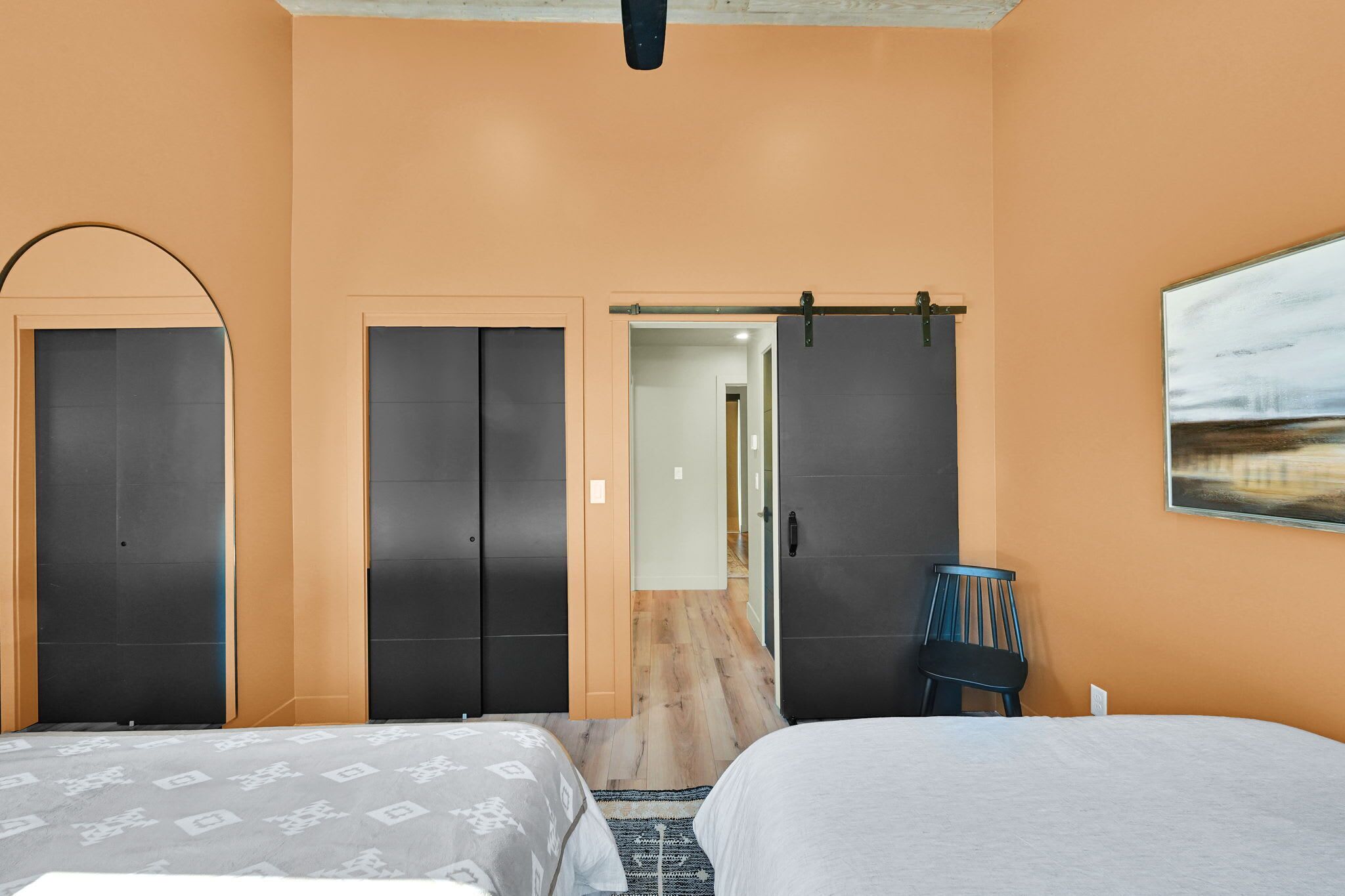 A hotel room with two beds, a wooden floor, a sliding door, a chair, and a painting on the wall.
