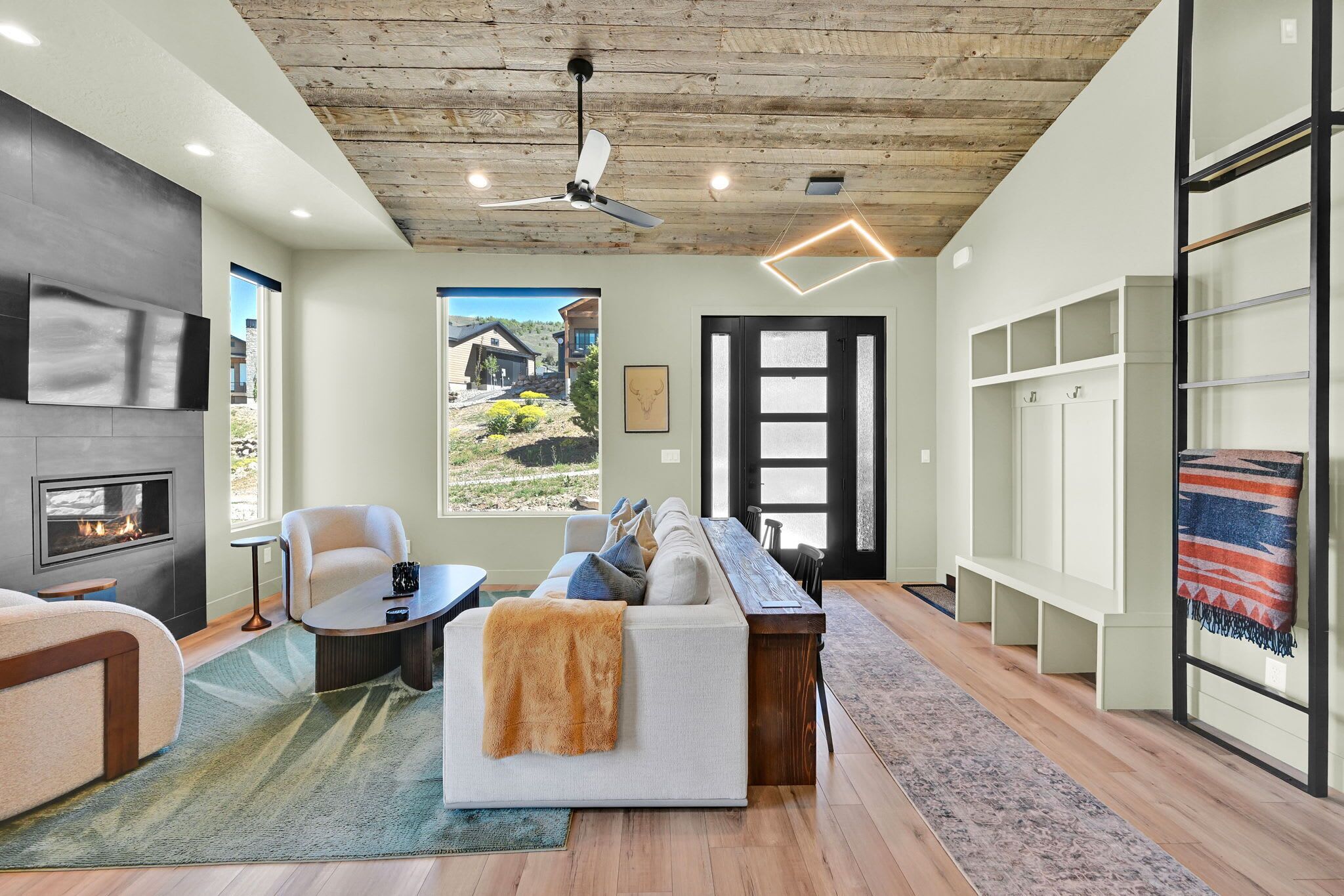 A modern living room with a fireplace, a sofa, a coffee table, and a view of a house through a large window.
