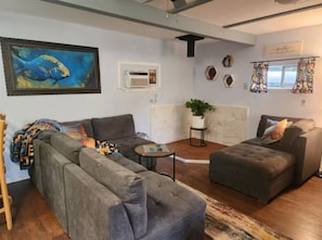 A living room with a sectional sofa, a small table, a potted plant, and a painting on the wall.