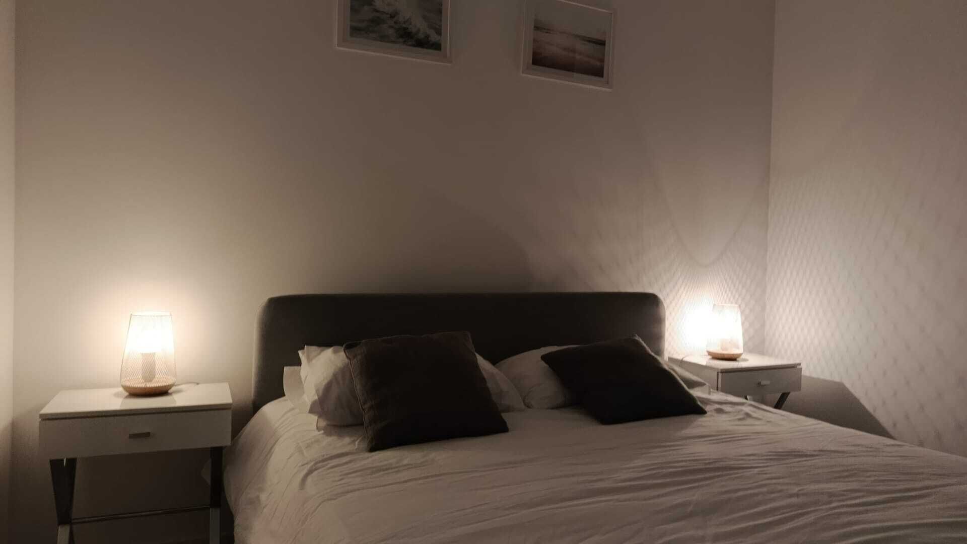 Un dormitorio con cama, dos mesitas de noche y dos lámparas de pared.