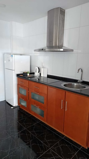Una cocina con extractor de acero inoxidable, un lavamanos, un refrigerador y una encimera con electrodomésticos.