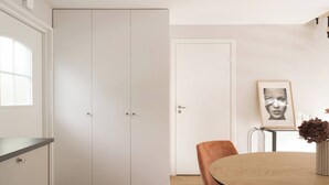 A room with a white wardrobe, a round table with a vase, and a framed picture on the wall.