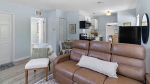 Een woonkamer met een bruine leren bank, een witte fauteuil en een eettafel met stoelen.