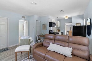 Ein Wohnzimmer mit brauner Ledersofa, einem weißen Sessel und einem Esstisch mit Stühlen.