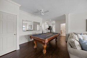 Ein Billardtisch in einem Raum mit weißen Wänden, einem Deckenventilator und einer Couch.