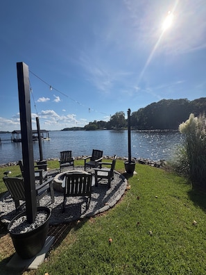 Ein Sitzbereich am Seeufer mit Adirondack-Stühlen, einer Feuerstelle und einem Steg, der ins Wasser führt.