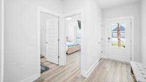 Een gang met witte wanden en houten vloeren die leidt naar een slaapkamer met een bed en een raam.