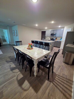 A dining area with a table and chairs, a kitchen with cabinets and appliances, and a hallway leading to another room. - Spacious 4 bedroom sleeps 10 one level house only minutes to the beach! (Foley)
