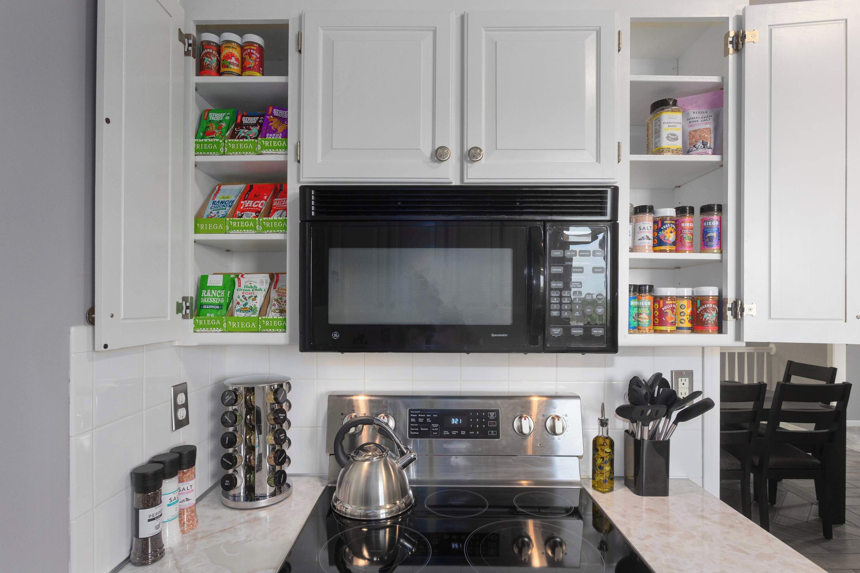 A kitchen with white cabinets, a black microwave, a stainless steel stove, and various kitchen utensils.