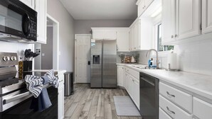 A modern kitchen with white cabinetry, stainless steel appliances, and a wooden floor.