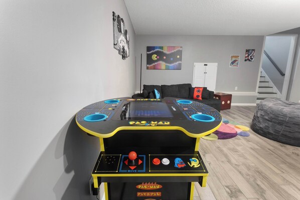 Pac-Man-peliautomaatti huoneessa, jossa on harmaa seinä, portaikko ja papupussi-istuin.
