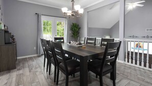 A dining area with a dark wooden table, six chairs, a chandelier, and a view of the outdoors through a window.
