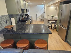 A modern kitchen with granite countertops, stainless steel appliances, and a central island with stools. - 5th Avenue All New Basement Suite (Lethbridge)