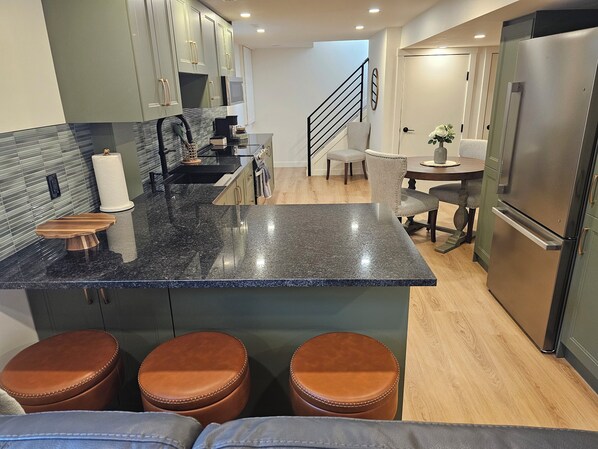 Eine moderne Küche mit Granit-Arbeitsplatten, Edelstahlgeräten und einer zentralen Kochinsel mit Hockern.