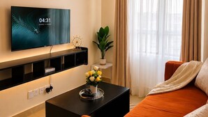 Una sala de estar moderna con una televisión de pantalla plana, una mesa de centro con un jarrón de flores, un sofá y un ventanal con cortinas.