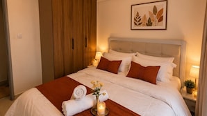 Una habitación de hotel con una cama grande, un armario de madera, una obra de arte con hojas en el pared y una mesita de noche con una lámpara.
