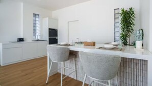 A modern kitchen with white cabinetry, a black refrigerator, and a bar area with two grey chairs. - New1BR Villa Private Pool in Uluwatu (Kuta)