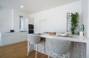 A modern kitchen with white cabinetry, a black refrigerator, and a bar area with two grey chairs. - New1BR Villa Private Pool in Uluwatu (Kuta)