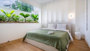 A bedroom with a bed, a bedside table, a wall-mounted plant shelf, and a window with a view of greenery. - New1BR Villa Private Pool in Uluwatu (Kuta)