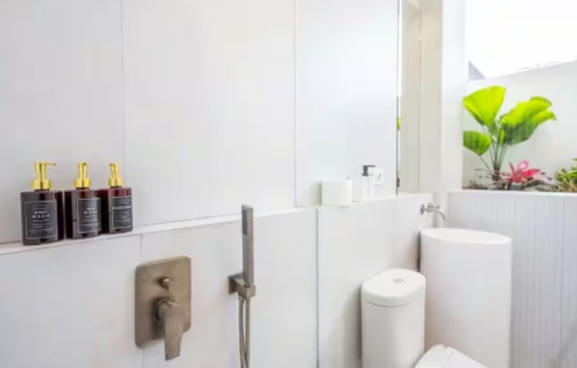 A modern bathroom with a shower, toilet, and sink. There are three toiletries on the wall.