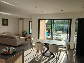 A modern living room with a sofa, dining table, chairs, and a view through large windows. - New villa in Périgord - Swimming pool & 5 mn from Sarlat center - family dream (Sarlat-la-Canéda)