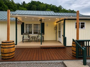Ein Holzhaus mit einer Veranda, zwei Stühlen, einem kleinen Tisch und zwei Fässern.