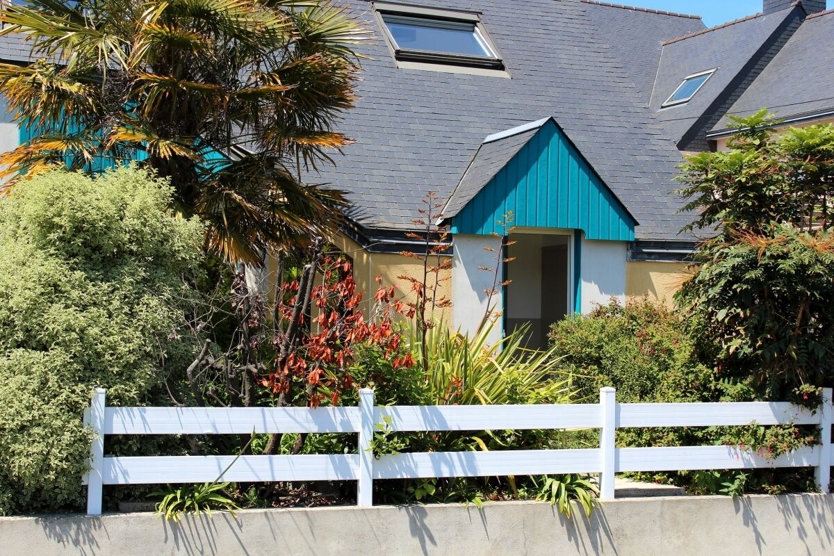 Een woongebouw met een blauw dak, een witte hek en verschillende planten.