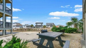 Een terras aan het strand met een picknicktafel, een houten terras en huizen op de achtergrond.