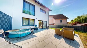 Ein modernes Haus mit Swimmingpool, Sitzgelegenheiten im Freien und einem großen Fenster.