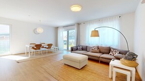 A modern living room with a sofa, ottoman, dining table, chairs, and a lamp. - Modern, spacious house with 5 bedrooms, 3 bathrooms and a large garden (Kindsbach)