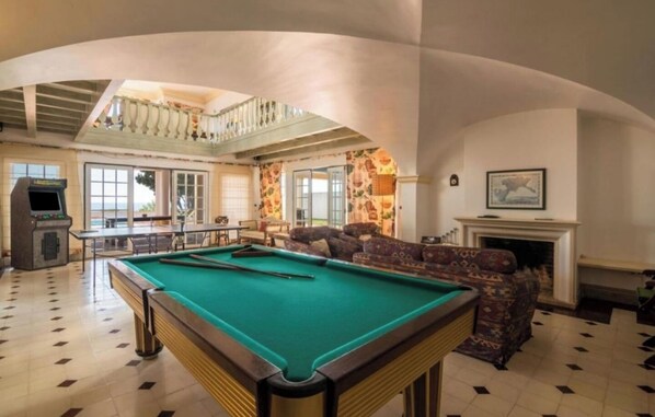 A pool table in a spacious room with a high ceiling, a fireplace, and a balcony with a railing. - VILA Bouganvila - V3 - Jacuzzi in top of the Sea (Albufeira)