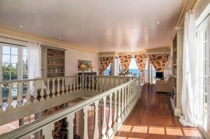 A spacious hallway with a wooden railing, bookshelves, and a view of the sea. - VILA Bouganvila - V3 - Jacuzzi in top of the Sea (Albufeira)