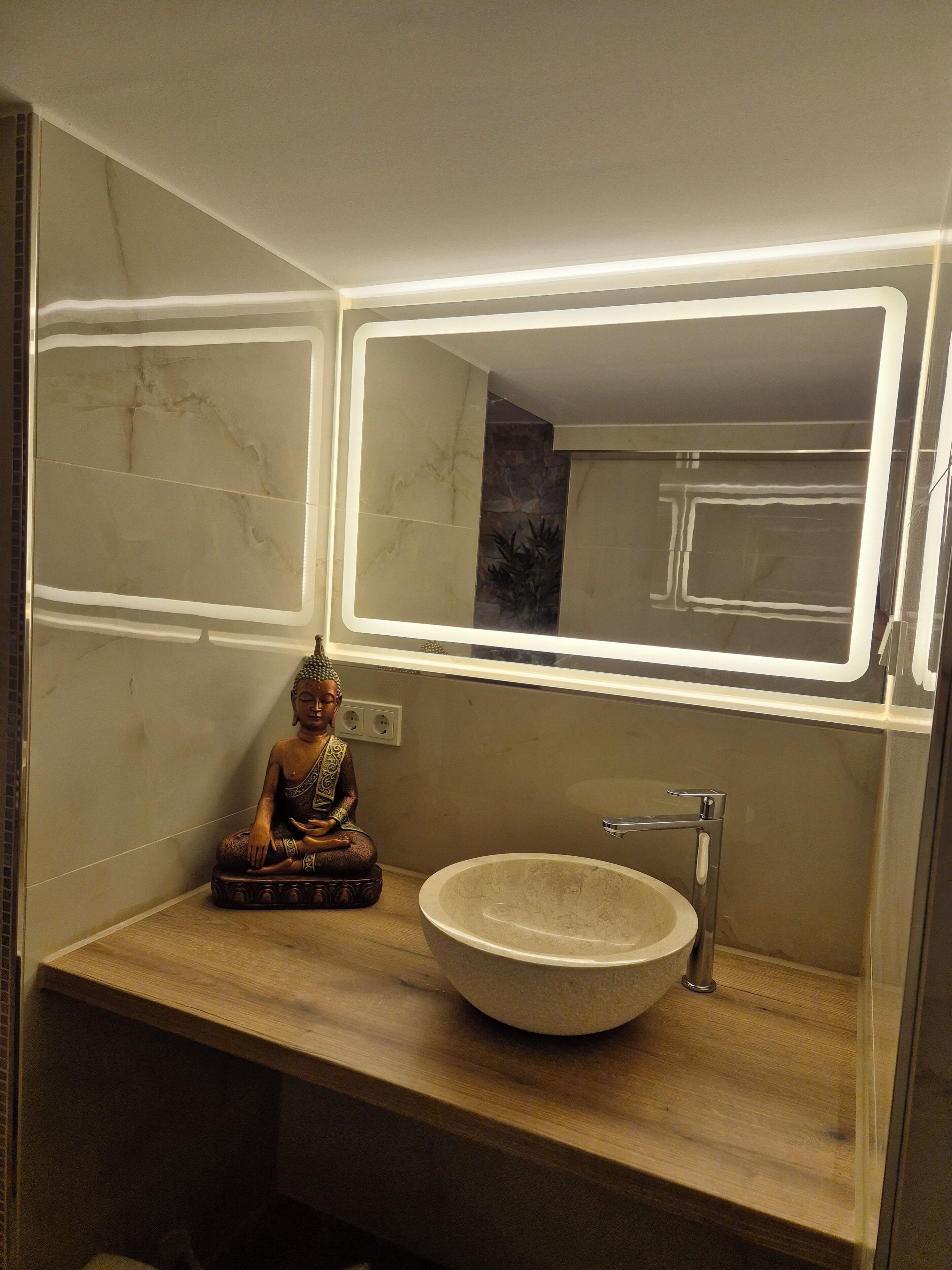 Un baño con tocador de madera, un lavabo redondo y una estatua de Buda.