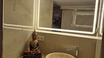Un baño con tocador de madera, un lavabo redondo y una estatua de Buda.