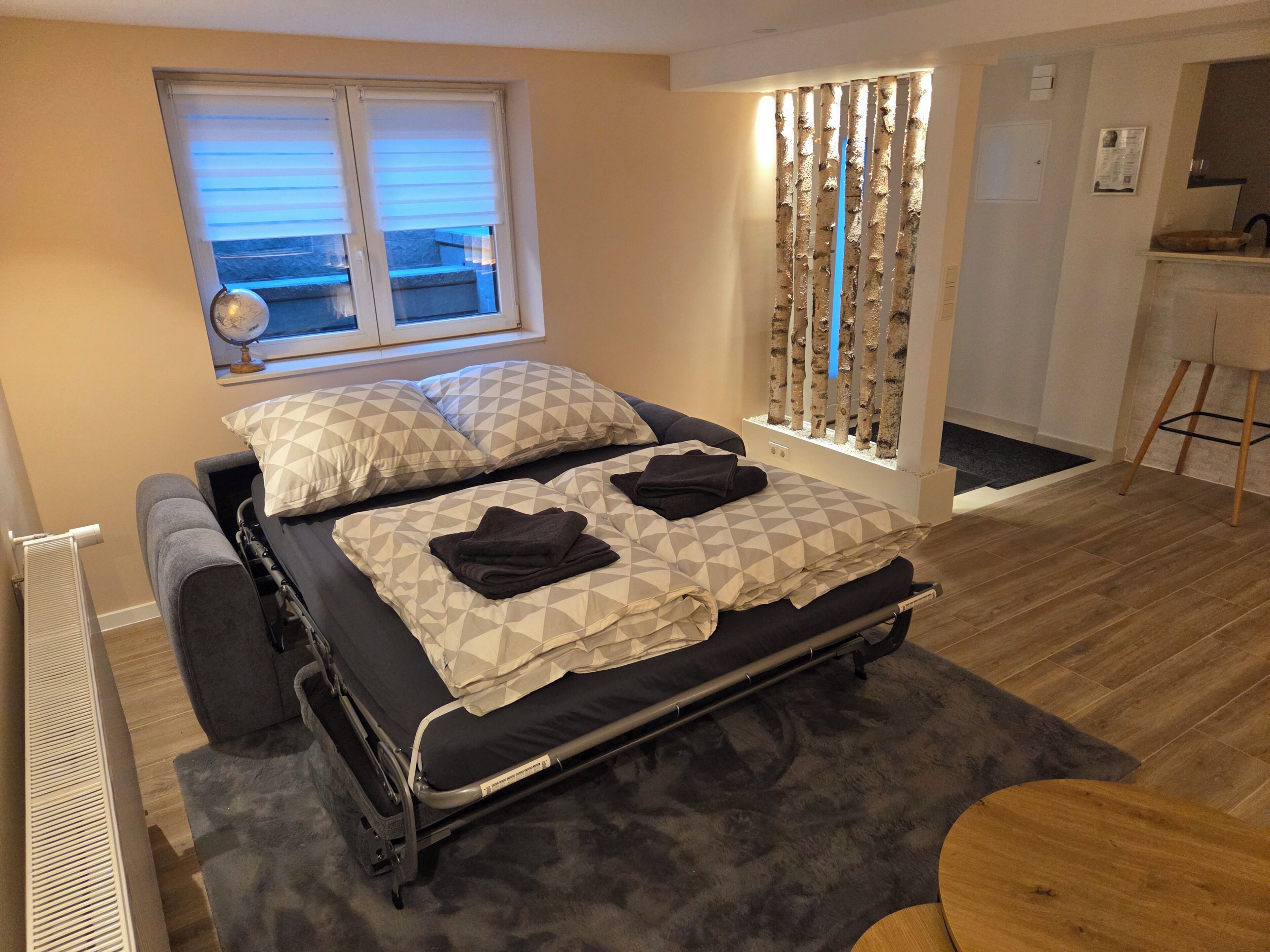 A bedroom with a bed, a window, a curtain, a radiator, a desk, and a chair.