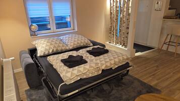 A bedroom with a bed, a window, a curtain, a radiator, a desk, and a chair.