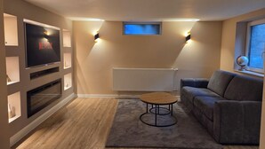 Uma sala de estar com televisão de tela plana, sofá, mesa de centro e luminárias fixadas na parede.