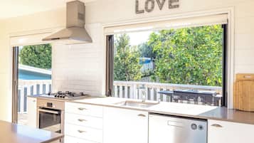 A modern kitchen with a gas stove, oven, and dishwasher, a large window with a view of greenery, and a 'LOVE' sign above the window.