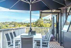 Un balcon avec une table et des chaises, un grand parasol et une vue sur un paysage vallonné.