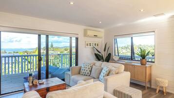A spacious living area with a large sliding glass door leading to a balcony, a sofa set, a wooden side table, and a small stool.