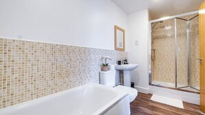 Een moderne badkamer met een witte badkuip, een douchecabine met glazen wanden en een witte wastafel.