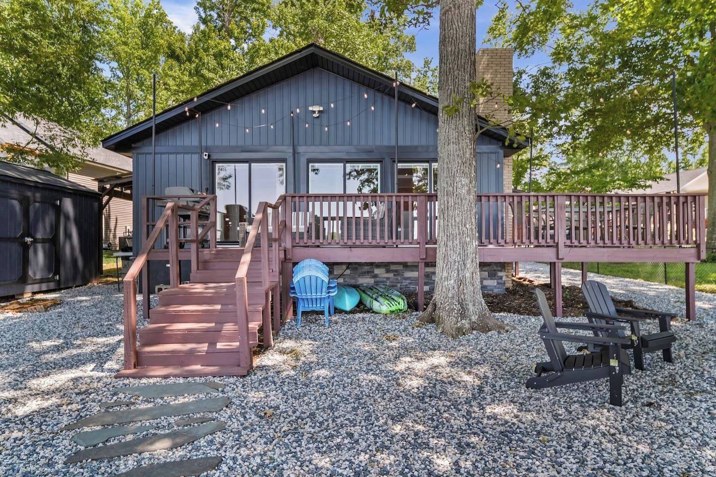 A cabin with a wooden deck, a staircase, and a tree in front.
