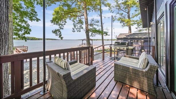 A deck with wicker furniture, a grill, and a view of a lake.