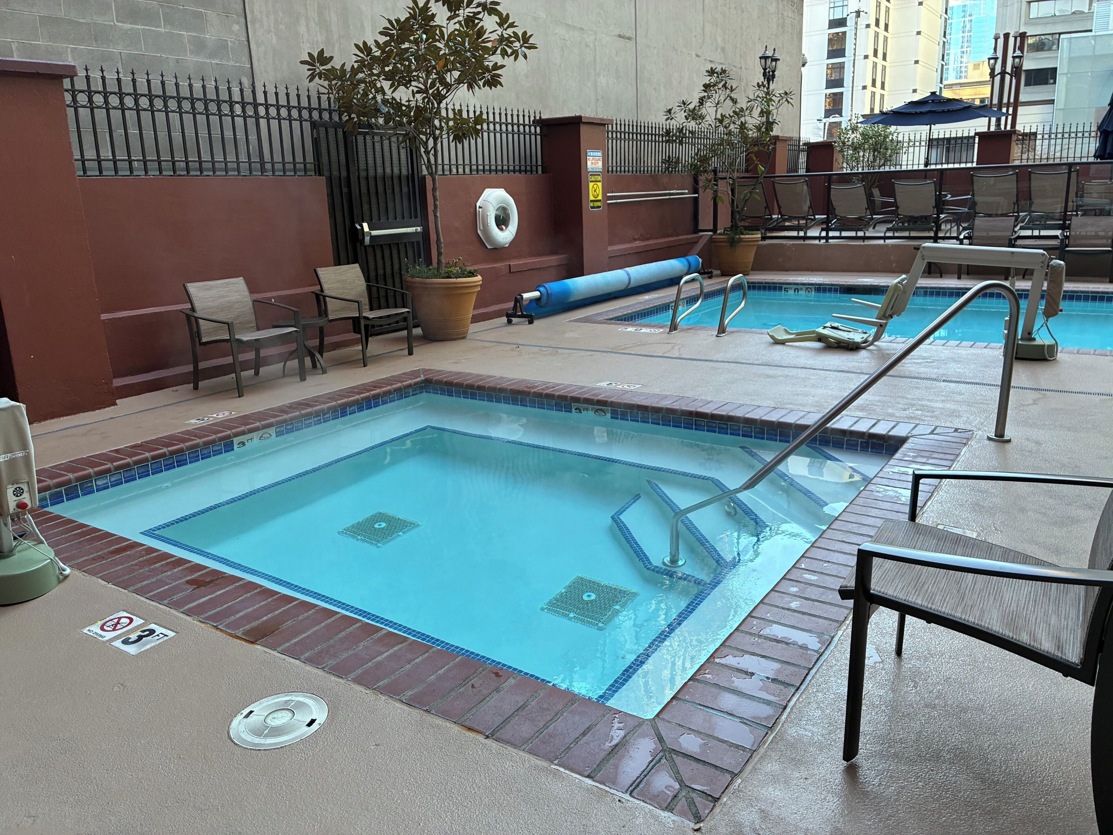 A pool area with two pools, chairs, and a small garden with potted plants.