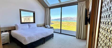 A bedroom with a large bed, a nightstand, a chair, and a view of a landscape through a sliding glass door.